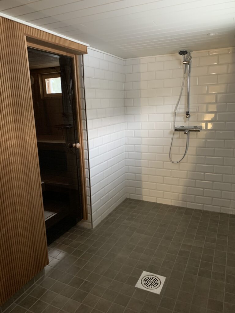 Harmahtava lattia laatta luo kontrastia valkoiseen seinälaattaan. Lämmin puupaneeli toimii myös äänen hallintaa jollin tilassa ei kaiu liikaa.
