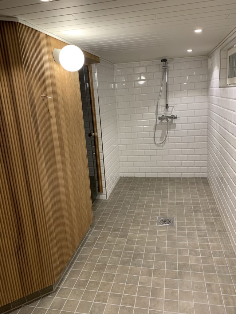 Sormipaneelilla paneloitu seinä luo lämpimän tunnelman muuten valkoisella kaakelilla laatoitettuun märkätilaan.